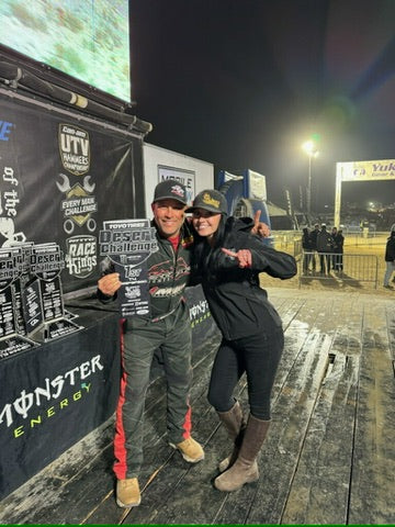 Two people posing in front of a Monster Energy branded booth at an event.