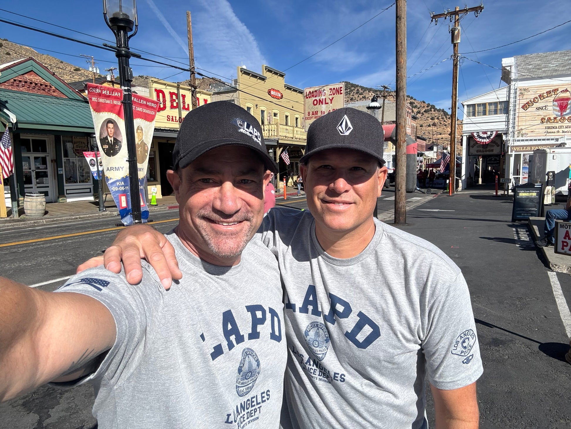 Two men taking a selfie on a street with buildings and signs in the background