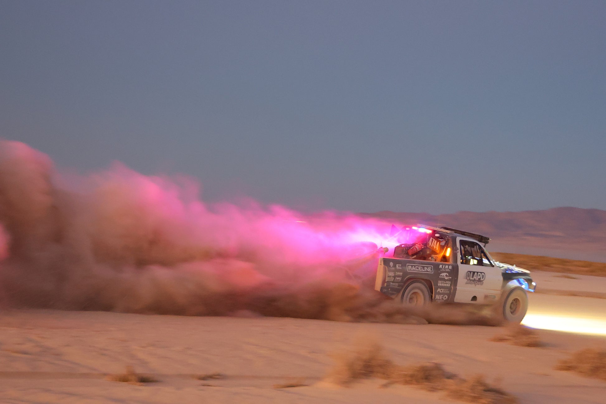 Off-road vehicle with pink exhaust in a desert at dusk