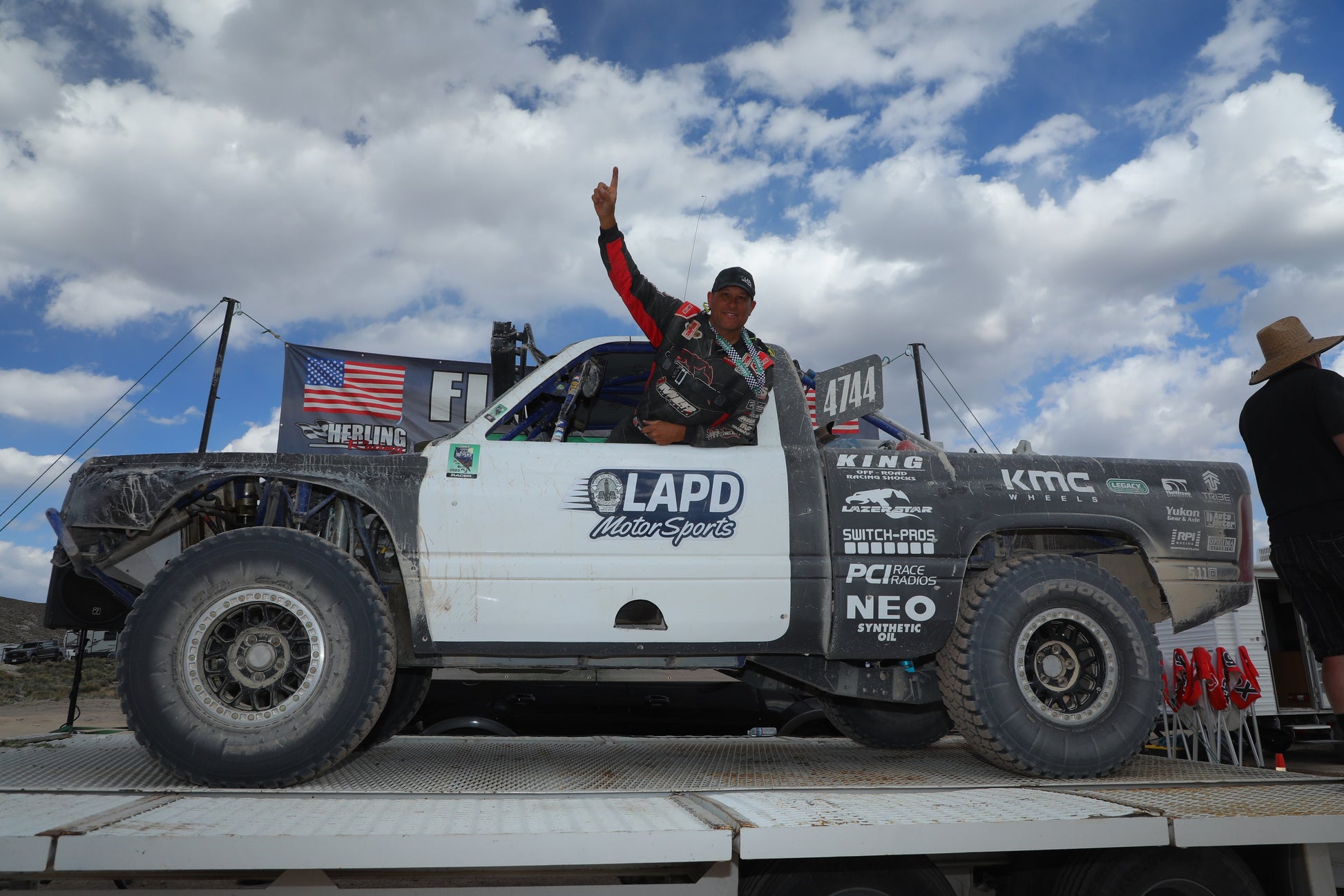 Monster truck with 'GAPD' branding on a flatbed truck against a cloudy sky.