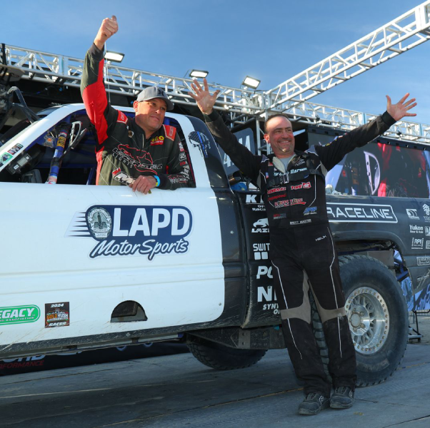 Two men celebrating in front of a race truck with LAPD Motor Sports branding.